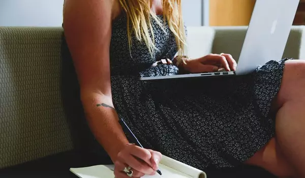 Person arbeitet am Laptop und schreibt sich etwas auf 